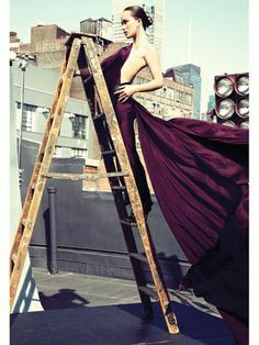 a woman in a long purple dress standing on top of a ladder with her back to the camera