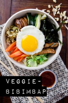 a bowl filled with vegetables, meat and an egg on top of it next to dipping sauce