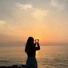 a woman standing on top of a beach next to the ocean holding a heart shaped object