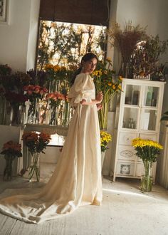 a woman standing in front of flowers wearing a long dress and holding a flower bouquet