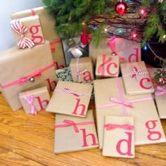 wrapped presents under a christmas tree with the word happy holidays spelled out on them in pink