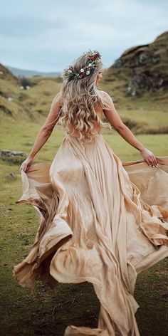 a woman in a long dress is walking through the grass with her back to the camera