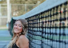 a woman leaning on the side of a tennis court holding a racquet and smiling