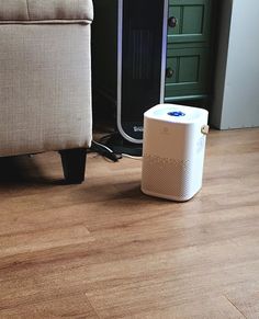 a white speaker sitting on top of a hard wood floor next to a beige chair