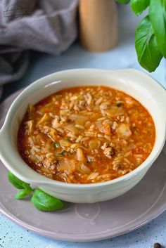 a white bowl filled with soup sitting on top of a plate next to a green plant