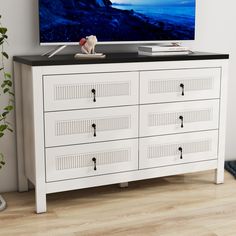 a white dresser with black top and drawers in front of a flat screen tv on the wall