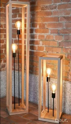 two wooden lamps sitting next to each other on a brick floor in front of a wall