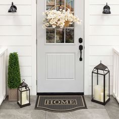 a front door with two lanterns and a wreath on the porch next to it that says home