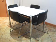 a white table with four black chairs around it on the tile floor in front of a door