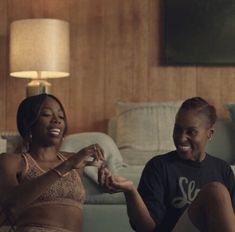 two women sitting on the floor in front of a couch and smiling at each other