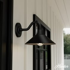 an outdoor wall light on the side of a house with white siding and black shutters