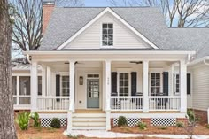 a white house with black shutters on the front porch and covered porches, surrounded by trees