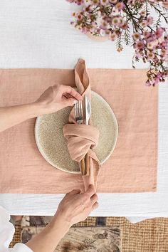 a person is setting a plate on a table with pink napkins and silverware