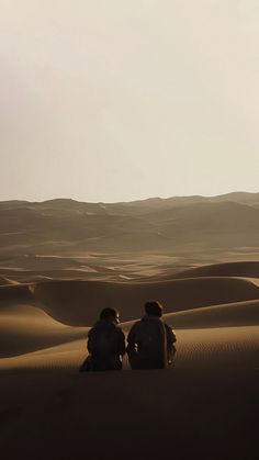 two people sitting on top of a sand dune