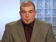 a man wearing a suit and tie sitting in front of a wall with glass blocks