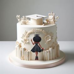 a decorated cake with a girl in a graduation cap and gown holding a book on top