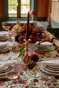 the table is set with plates, silverware and red flowers in glass vases