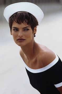 a woman with short hair wearing a sailor's hat and black swimsuit on the beach