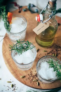 three glasses filled with ice and herbs on top of a wooden tray next to bottles