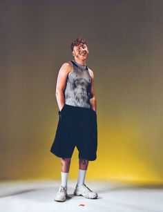 a man standing in front of a yellow background wearing black shorts and a tank top