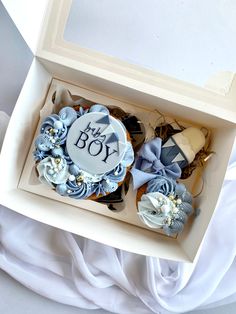 two decorated cupcakes in a white box with blue ribbons and bows on top