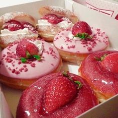 four donuts with pink icing and strawberries in a box