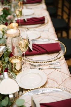 a long table is set with place settings and silverware, red napkins, and gold rimmed glasses