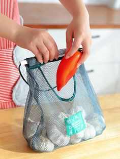 a person holding a carrot in a mesh bag on a wooden counter top next to an oven