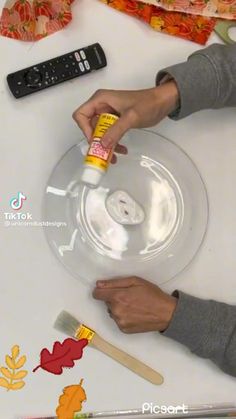 a person is painting a glass plate with acrylic paint and some autumn leaves