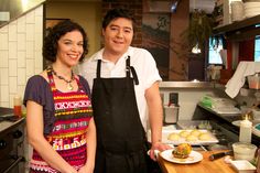 a man and woman standing next to each other in a kitchen with food on the counter