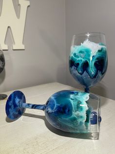 two wine glasses sitting on top of a table next to each other with blue and white swirled liquid in them