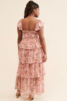 a woman wearing a pink floral print dress with ruffles on the bottom and back