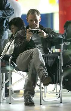 a man sitting in a chair holding a camera and taking a photo with his cell phone