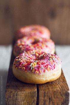 two donuts with sprinkles are sitting on a wooden board by jodi lenski for stocksy