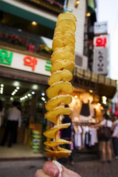 a person holding up a donut on a stick in front of a storefront