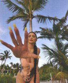 a woman in a bathing suit holding her hand up to the sky with palm trees behind her