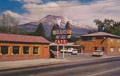 a motel with mountains in the background and cars parked on the side of the road