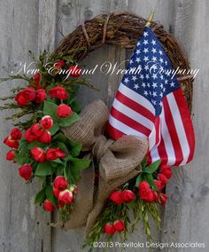 a wreath with flowers and an american flag hanging on the side of a wooden fence