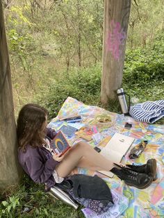 a young woman sitting on top of a blanket next to a forest filled with trees