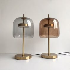 two glass lamps sitting on top of a white table next to each other and one has a gold metal base