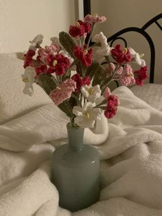 a blue vase filled with pink and white flowers on top of a bed covered in blankets