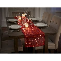 the table is set with white plates and silverware on it, lighted by candles