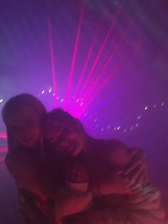 two girls are hugging in front of purple lights