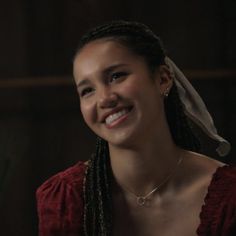 a woman with braids smiling and wearing a red dress in the dark, she has a white bandana on her head