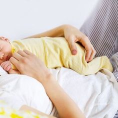 a woman holding a baby in her arms while laying on a bed with white sheets