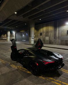 a black sports car parked in an empty parking garage with its doors open at night