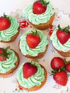 some cupcakes with green frosting and strawberries on top are sitting on a plate