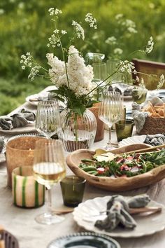 a table set with plates, glasses and vases filled with flowers on top of it