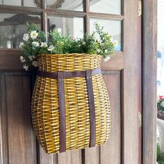 a wicker basket hanging on the front door with flowers in it and an attached handle