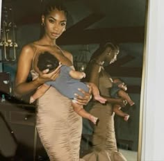 a woman holding a baby in her arms while standing next to two other women wearing dresses